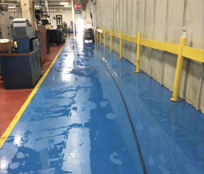Commercial warehouse facility with blue flooring pooled with water after a loss.