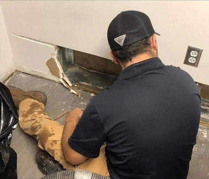 Man sitting on the floor, looking at a wall baseboard, baseboard has been removed due to water damage